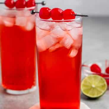 red drink in a tall clear glass with cherries on top.