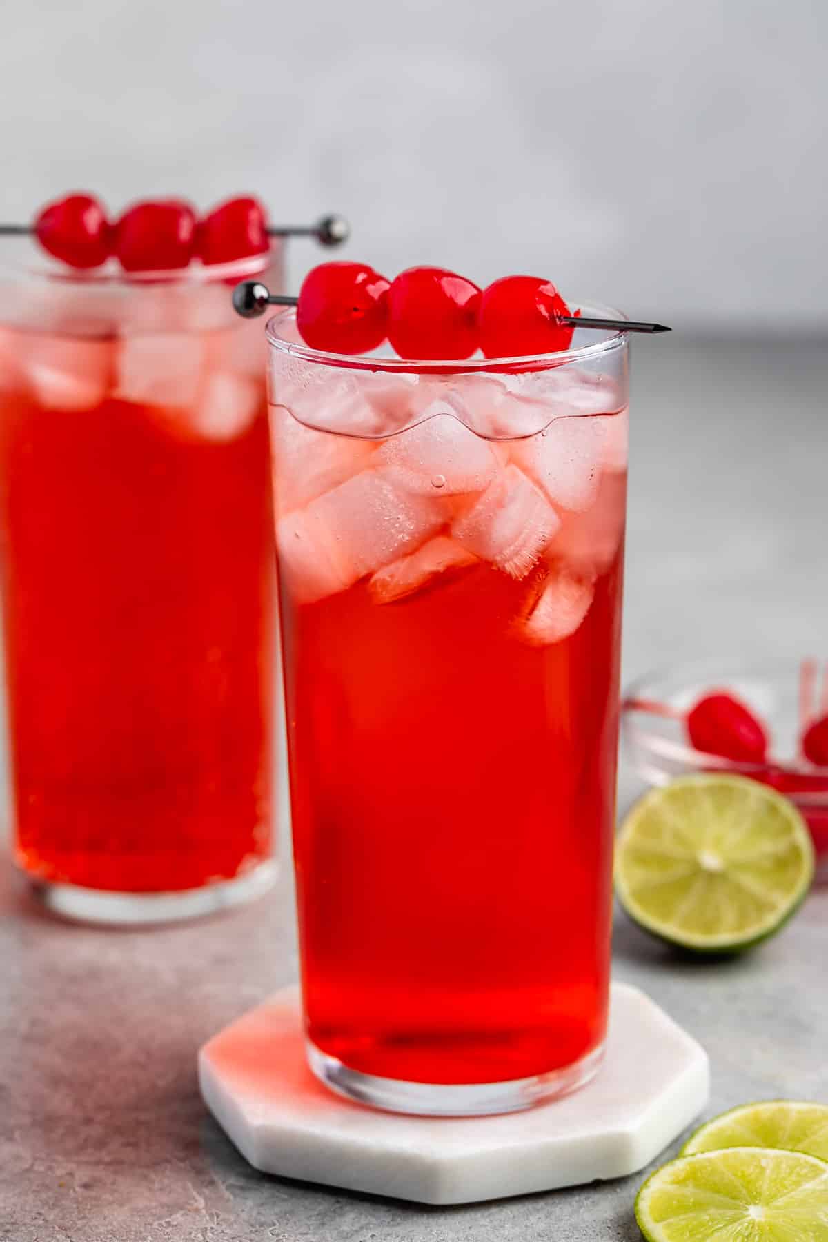 red drink in a tall clear glass with cherries on top.