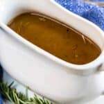 brown gravy in a white gravy boat next to rosemary