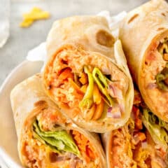 A close-up of a plate with several halved wraps. The wraps are filled with shredded chicken, lettuce, carrots, and red onion, all mixed in a creamy orange sauce. The tortilla is lightly toasted and golden brown.