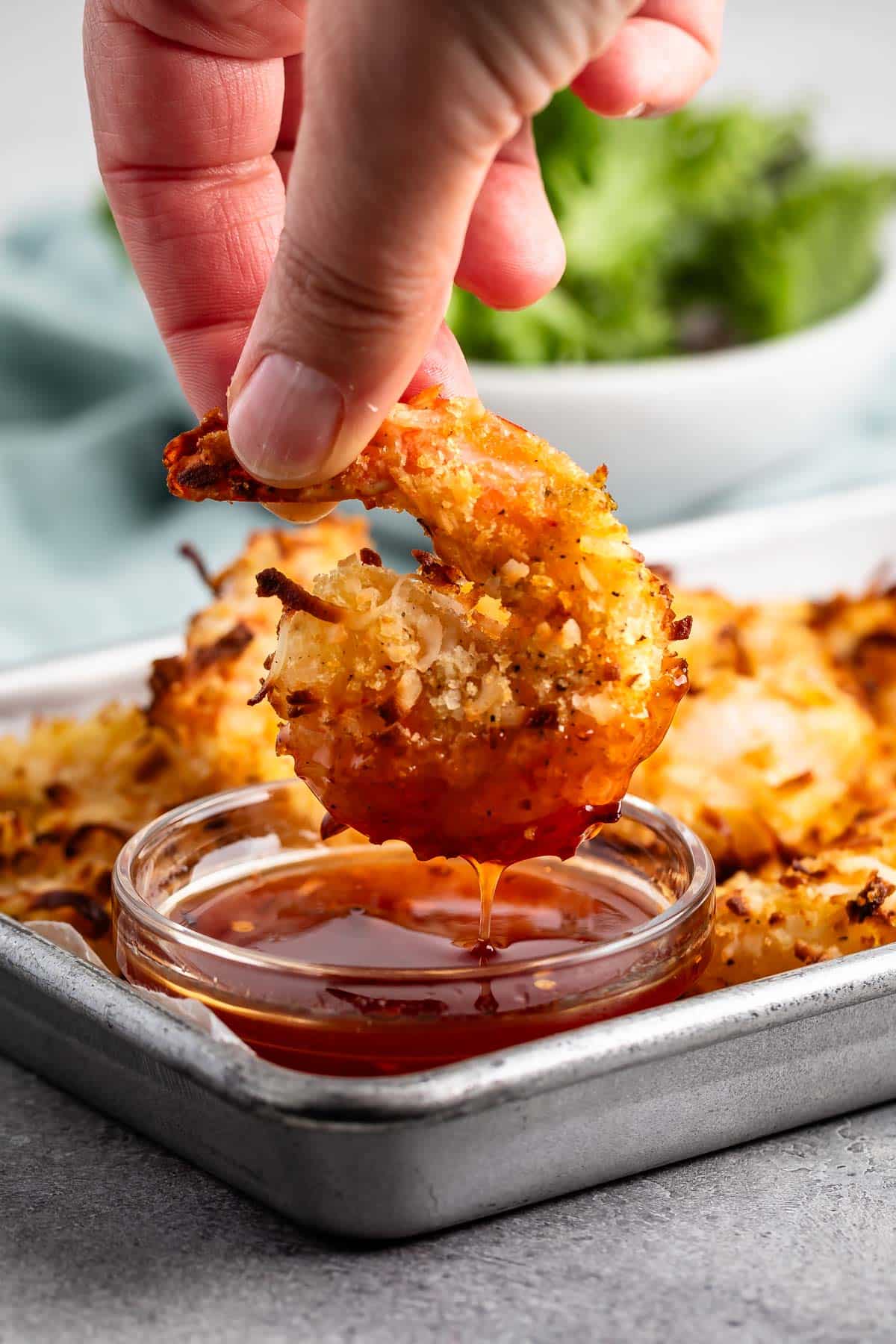 hand holding shrimp on a pan next to a sauce.