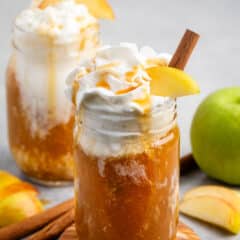 apple cider and whipped cream in a clear mason jar with caramel sauce and sliced apples on top.