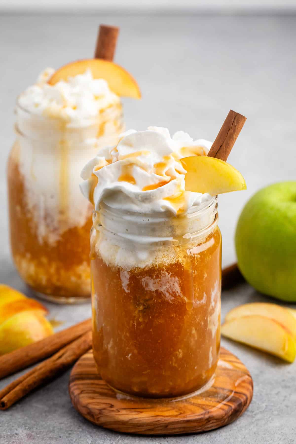 apple cider and whipped cream in a clear mason jar with caramel sauce and sliced apples on top.