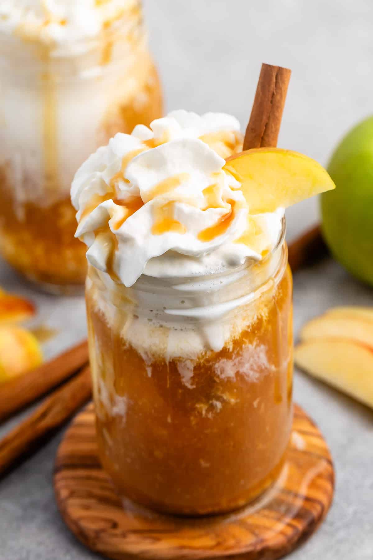 apple cider and whipped cream in a clear mason jar with caramel sauce and sliced apples on top.