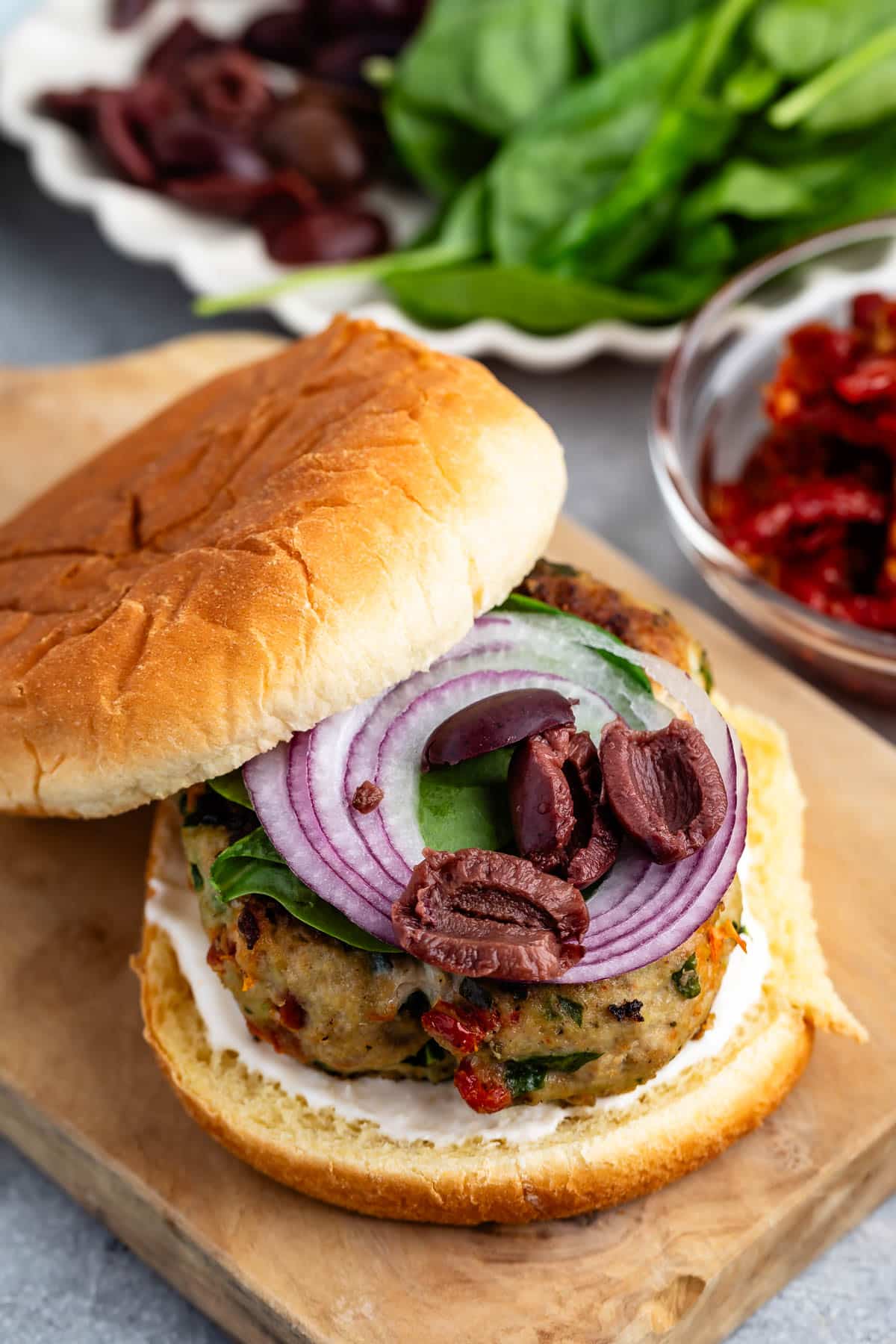 turkey burger on a cutting board topped with onions and spinach and buns.