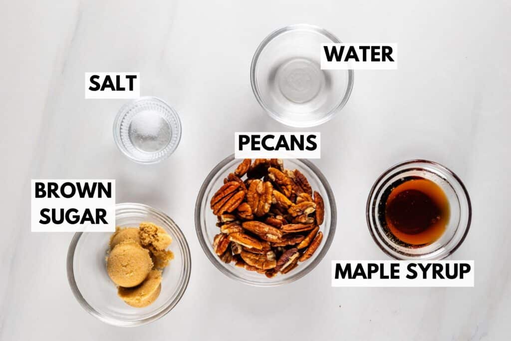 Various ingredients in separate glass bowls on a white surface, labeled: Salt, Brown Sugar, Pecans, Water, and Maple Syrup.