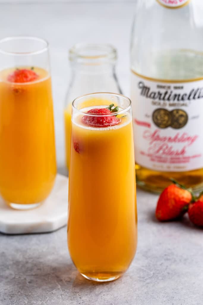 virgin mimosa in a tall clear glass with a strawberry floating in the drink.