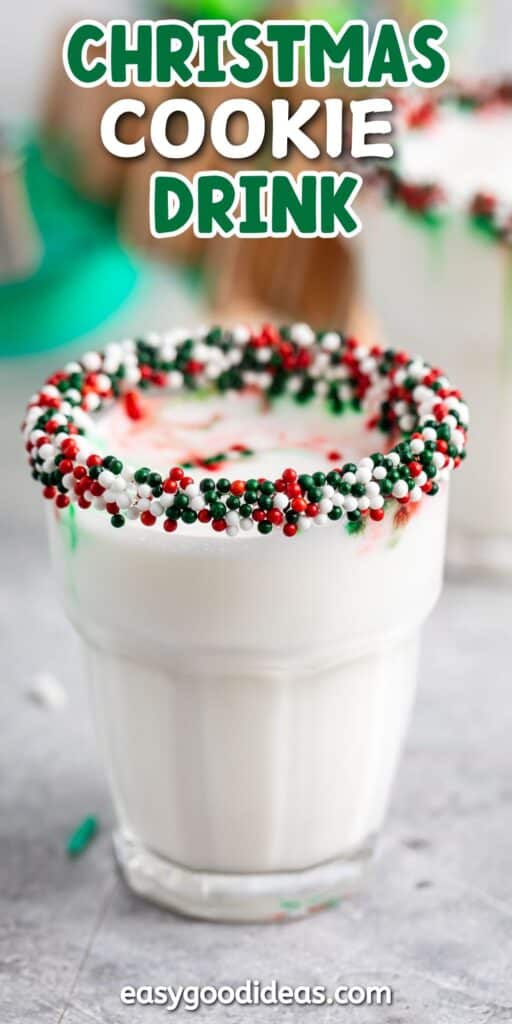 A glass of creamy white milkshake with a rim decorated in vibrant red, green, and white sprinkles. The background is slightly blurred, enhancing the focus on the festive drink.