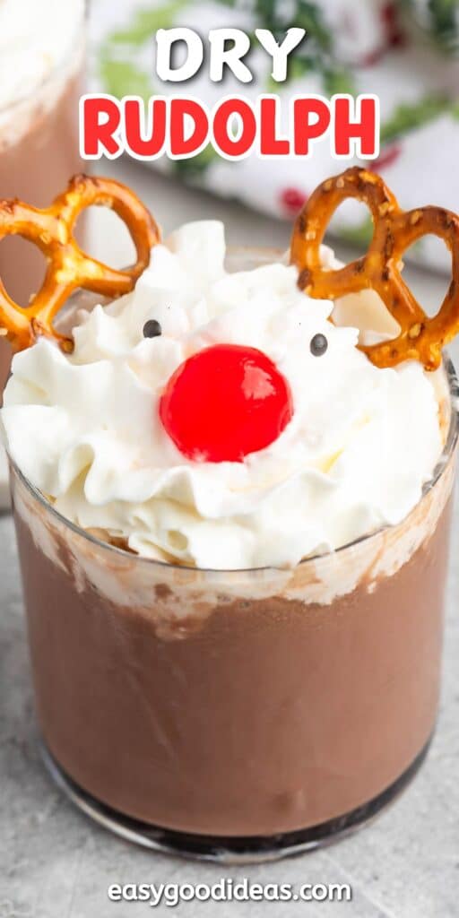 A festive drink with whipped cream topped with a red cherry and two pretzels resembling a reindeer face. Text at the top reads Dry Rudolph. The drink is served in a clear glass.