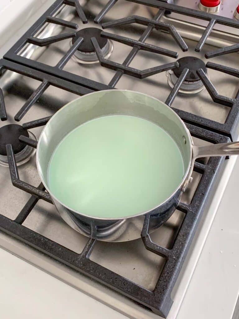 A silver pot filled with a light green liquid is positioned on a metal stove with four burners.