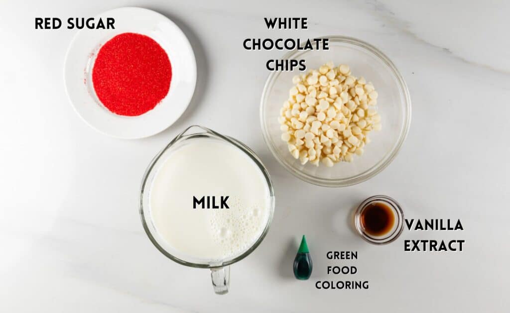 Ingredients on a white surface: a bowl of red sugar, a bowl of white chocolate chips, a glass cup of milk, a small bottle of green food coloring, and a small container of vanilla extract.