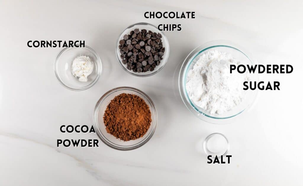 Overhead view of baking ingredients on a white surface: a bowl of powdered sugar, a bowl of chocolate chips, a small bowl of salt, a bowl of cocoa powder, and a bowl of cornstarch. Each ingredient is labeled in bold text.