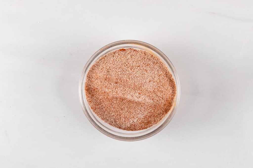 A top-down view of a round glass container filled with a fine, light brown powder, placed on a white marble surface.