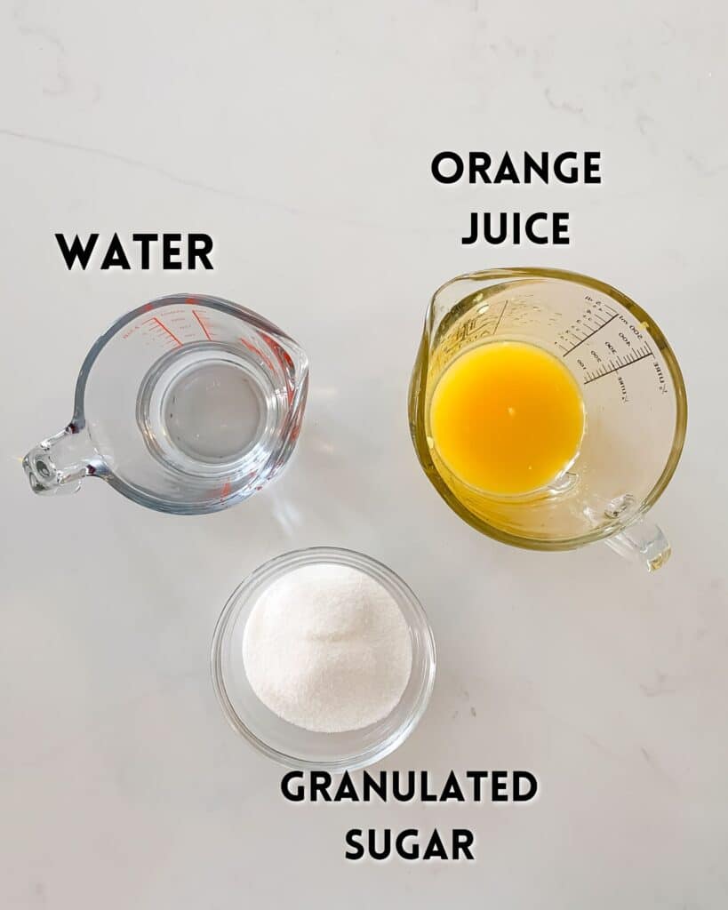 A clear measuring cup with water, a glass jug with orange juice, and a small bowl of granulated sugar are arranged on a white surface. Labels indicate each items contents.