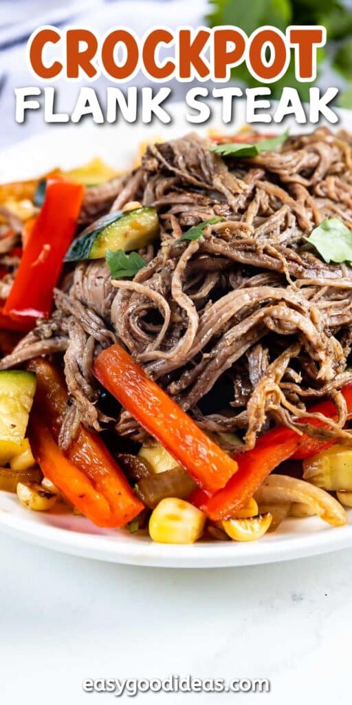 A close-up of shredded flank steak served with sliced red bell peppers, zucchini, and corn. The food is arranged on a white plate, garnished with fresh herbs. Text at the top reads Crockpot Flank Steak.