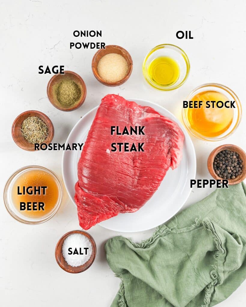 Raw flank steak on a white plate surrounded by small bowls of spices and ingredients, including oil, beef stock, onion powder, sage, rosemary, light beer, pepper, and salt. A green cloth is draped at the bottom.