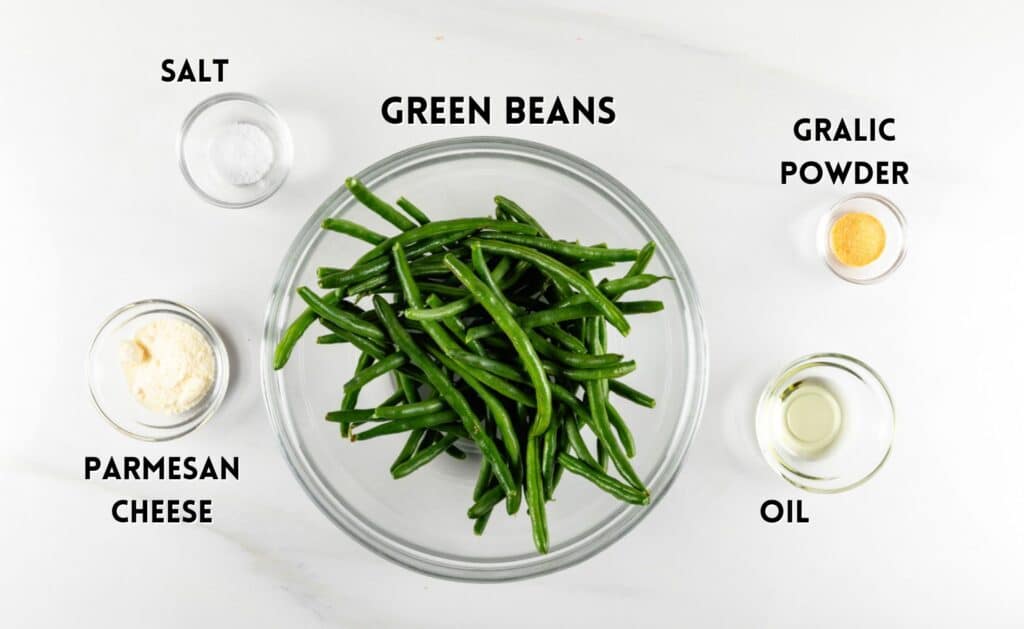 A glass bowl of fresh green beans is centered in the image, surrounded by small bowls containing salt, grated Parmesan cheese, garlic powder, and oil. Each ingredient is labeled with text above or beside the bowls.