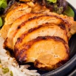 Grilled chicken slices on a plate with white rice and a fresh salad garnish, featuring lettuce and a crouton.