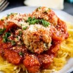 A plate of spaghetti squash topped with meatballs, marinara sauce, and sprinkled with grated Parmesan cheese and fresh parsley.