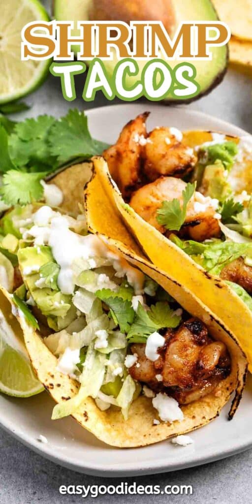 Two shrimp tacos filled with grilled shrimp, avocado, lettuce, crumbled cheese, and cilantro in corn tortillas. A lime wedge is on the side. The text Shrimp Tacos appears at the top, and easygoodideas.com is at the bottom.