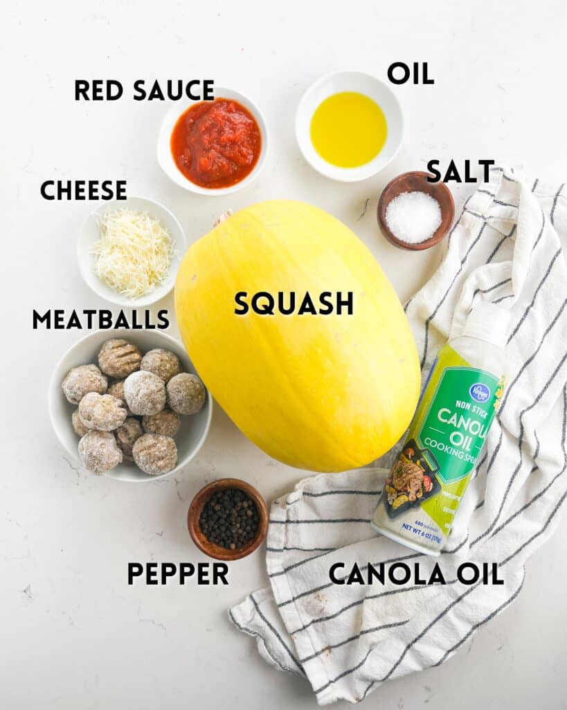 Ingredients for a squash dish arranged on a white surface: a spaghetti squash, a bowl of red sauce, grated cheese, meatballs, oil, salt, pepper, a striped cloth, and a can of canola oil cooking spray, with labels for each item.