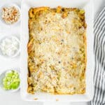 A baked casserole topped with grated cheese in a white dish. To the side, there are small bowls containing chopped celery, onions, and bread cubes. A striped cloth napkin is partially visible on the right.