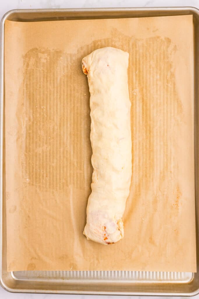A long roll of dough rests on a baking sheet lined with parchment paper. The dough is lightly browned and appears ready to be baked.