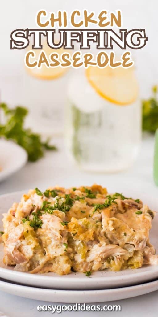 A serving of chicken stuffing casserole on a white plate, garnished with chopped herbs. A glass of lemon water and some greens are blurred in the background. Text reads Chicken Stuffing Casserole and easygoodideas.com.