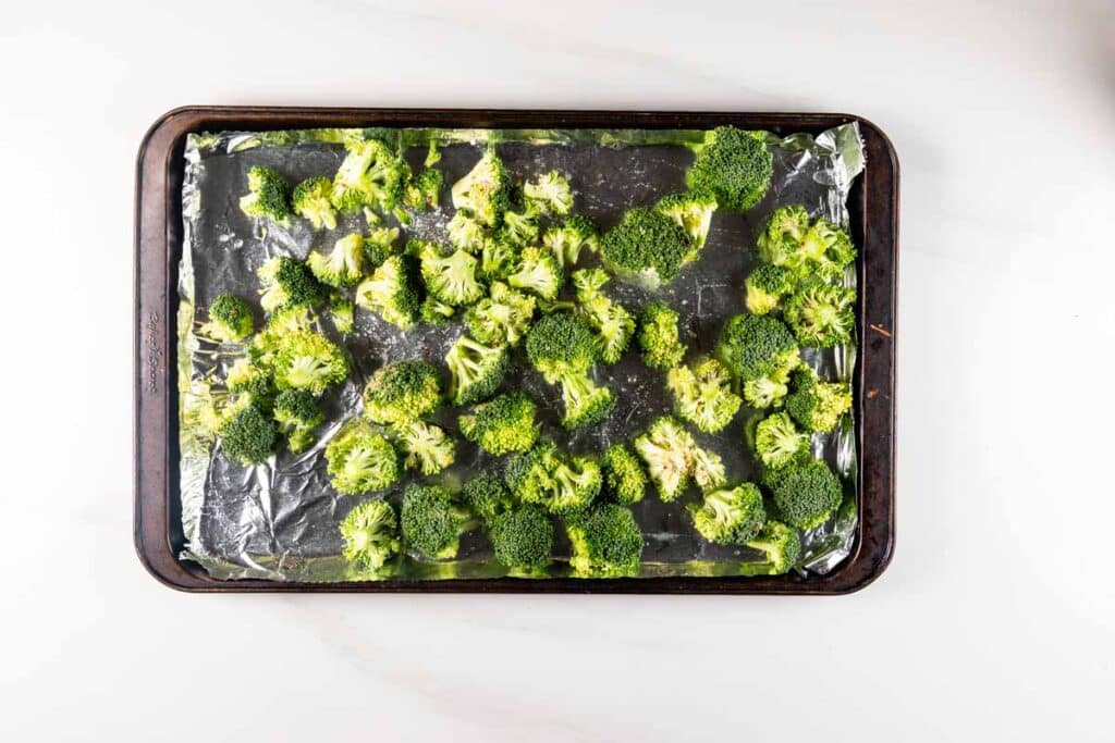 Overhead view of a baking tray lined with aluminum foil, filled with evenly spread broccoli florets, ready for roasting.