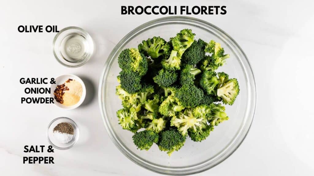 A glass bowl filled with broccoli florets is centered on a white surface. Nearby, small bowls contain olive oil, garlic and onion powder, and salt and pepper. Text labels each ingredient.