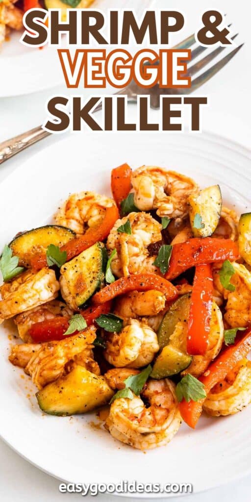 A white plate filled with shrimp and mixed vegetables, including zucchini and red bell peppers, garnished with herbs. A fork rests beside the plate. Text on top reads Shrimp & Veggie Skillet, with easygoodideas.com at the bottom.