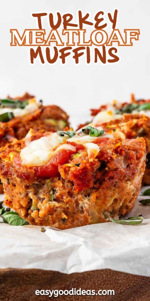 Close-up of turkey meatloaf muffins topped with tomato sauce and melted cheese. Garnished with herbs, they sit on a piece of parchment paper. Text at the top reads, Turkey Meatloaf Muffins and at the bottom is the website easygoodideas.com.