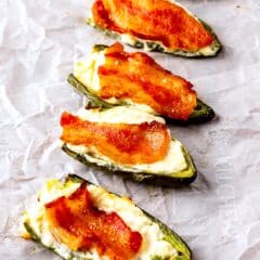 jalapeños covered in cream cheese and bacon laid out on parchment paper.