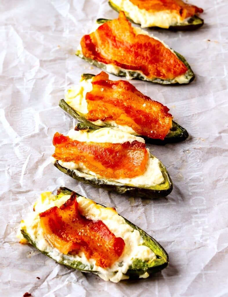 jalapeños covered in cream cheese and bacon laid out on parchment paper.