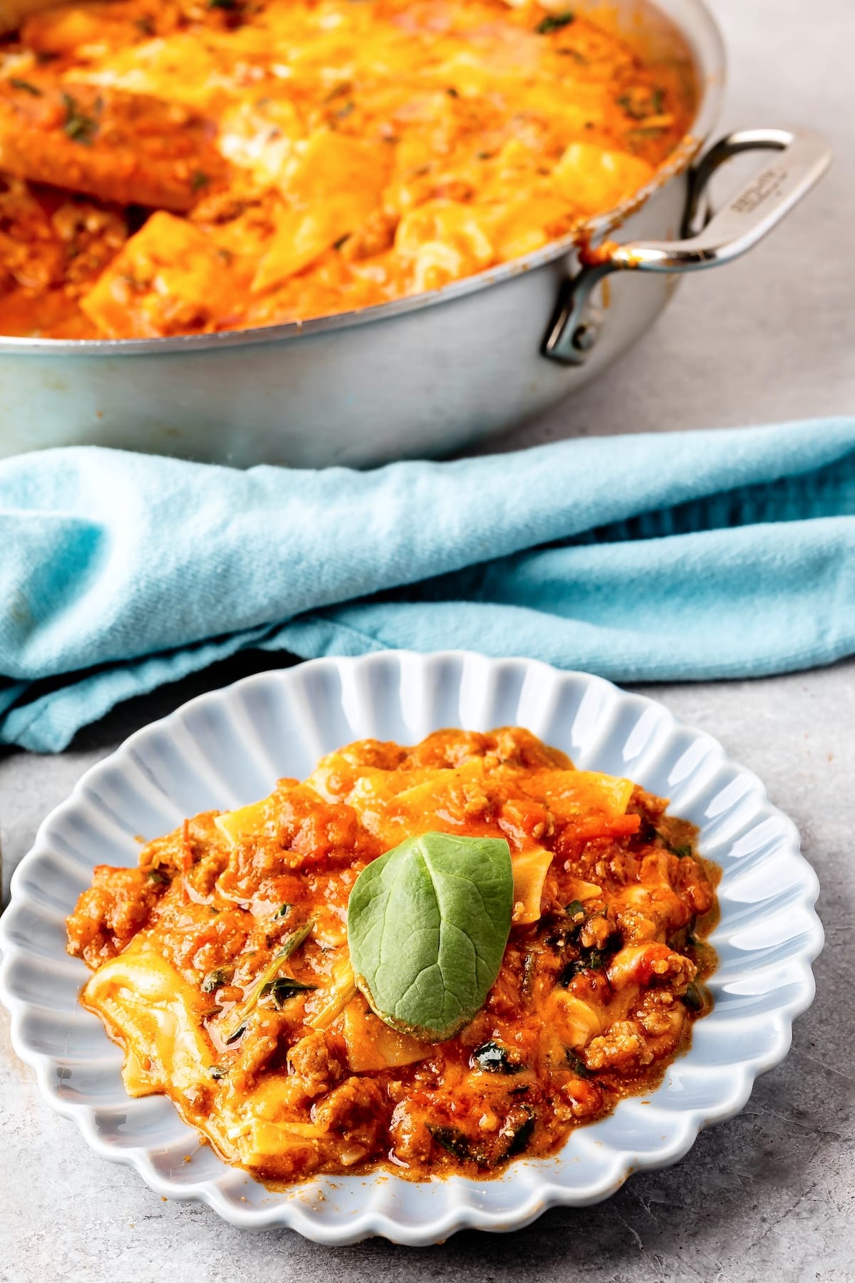 skillet lasagna on a grey plate with some green garnish on top and with more lasagna in the background.