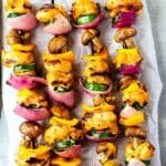 Skewers of grilled chicken, bell peppers, zucchini, red onions, and mushrooms, arranged on parchment paper. The vegetables and chicken are charred, showcasing a colorful and appetizing presentation.