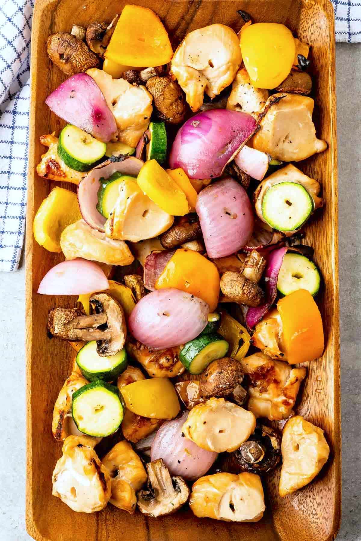 A colorful assortment of grilled chicken kabobs with pieces of chicken, yellow and green zucchini, red onions, mushrooms, and yellow bell peppers.