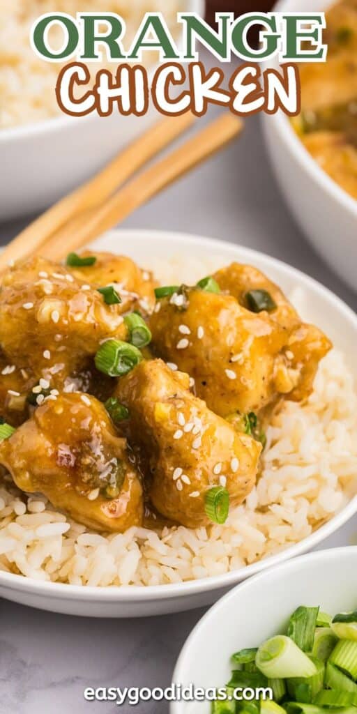 A bowl of orange chicken garnished with green onions and sesame seeds is served on rice. Wooden chopsticks rest on the bowls rim. A small dish with sliced green onions is nearby. The text Orange Chicken is at the top and easygoodideas.com at the bottom.