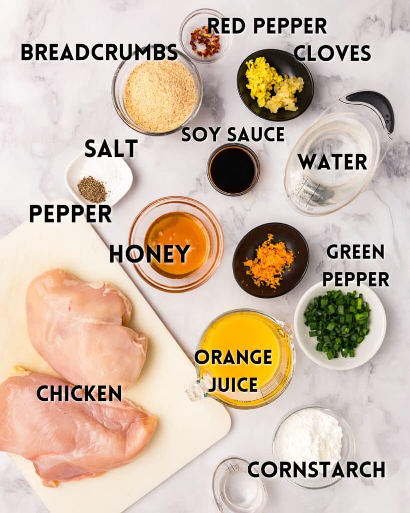 Ingredients are arranged on a marble surface: Breadcrumbs, red pepper flakes, cloves, soy sauce, water, salt, minced garlic, honey, orange juice, green pepper, pepper, chicken breasts, and cornstarch.