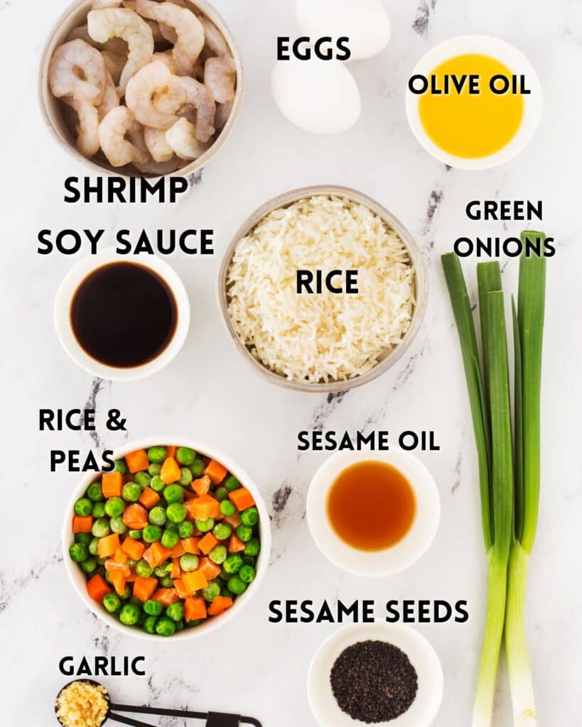 Ingredients for a dish are arranged on a white surface: shrimp, eggs, olive oil, rice, green onions, soy sauce, rice and peas mix, sesame oil, sesame seeds, and garlic.