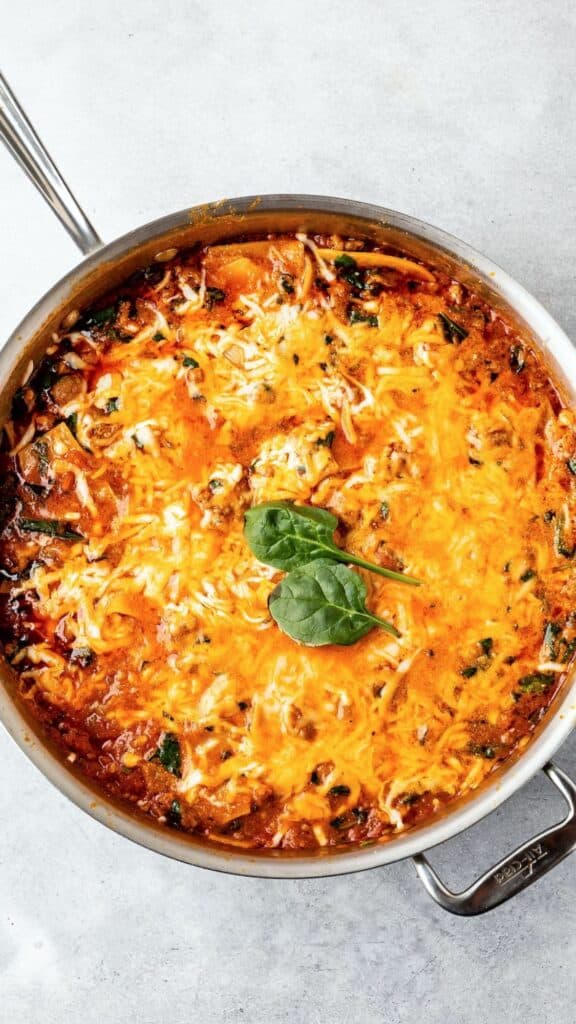 skillet lasagna in a silver skillet pan with some green garnish on top.