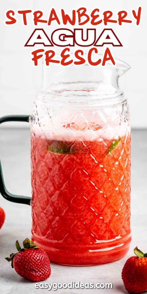 A glass pitcher filled with strawberry agua fresca, featuring a textured pattern and a handle. Fresh strawberries are placed around the pitcher. Red and white text at the top reads Strawberry Agua Fresca. Text at the bottom says easygoodideas.com.