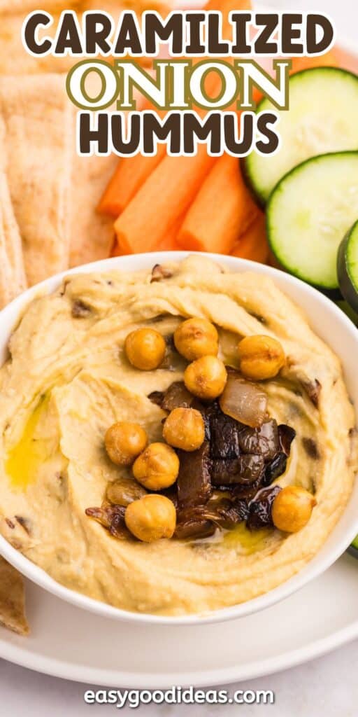 A bowl of caramelized onion hummus topped with whole chickpeas and caramelized onions, served with sliced cucumbers, carrots, and pita bread. Text above reads Caramelized Onion Hummus.
