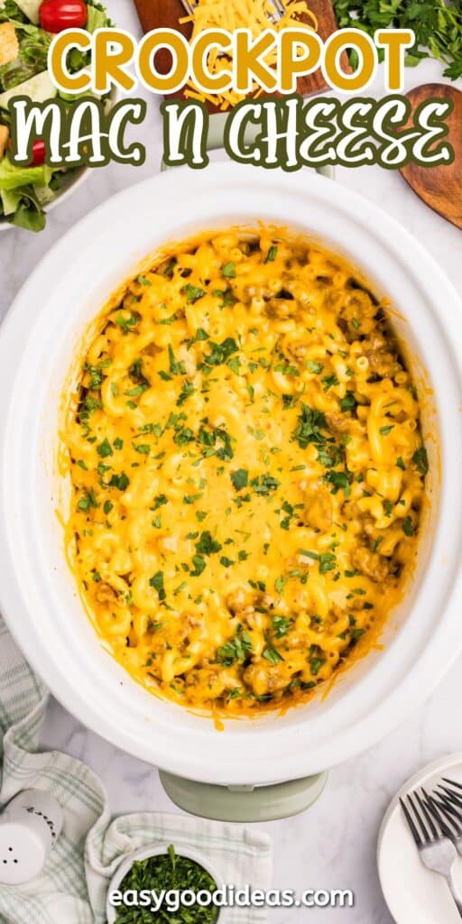 Overhead view of creamy macaroni and cheese in a crockpot, topped with chopped parsley. Text at the top reads “Crockpot Mac N Cheese,” and “easygoodideas.com” is at the bottom. Kitchen items surround the crockpot.
