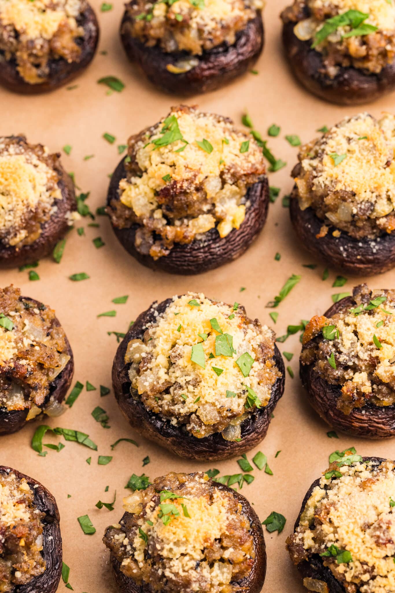 A plate of stuffed mushrooms topped with breadcrumbs and chopped herbs sits on a table, with stacked plates and a striped towel in the background.