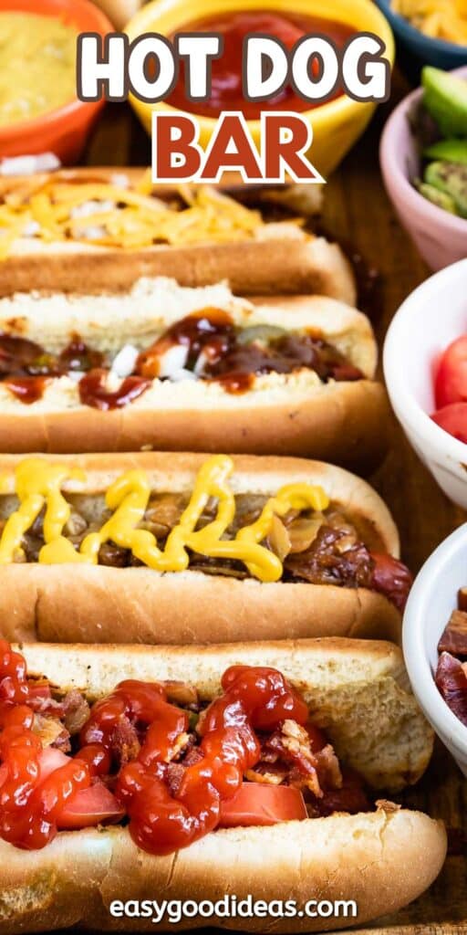 Four hot dogs with different toppings, including ketchup, mustard, and relish, are arranged on a wooden table surrounded by bowls of various condiments and toppings. HOT DOG BAR is written at the top in bold letters.
