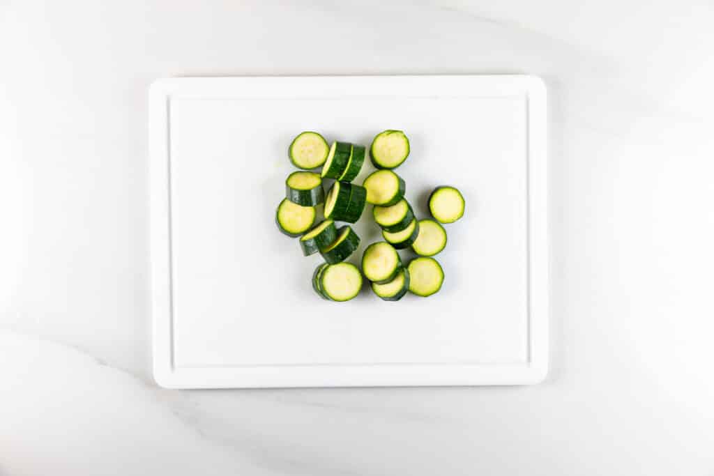 Sliced zucchini pieces arranged in the center of a white cutting board on a white countertop.