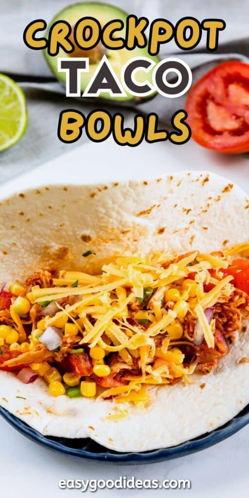 A flour tortilla filled with shredded chicken, corn, diced tomatoes, onions, and shredded cheese sits on a plate. Sliced lime and tomato are in the background. Text reads Crockpot Taco Bowls and easygoodideas.com.