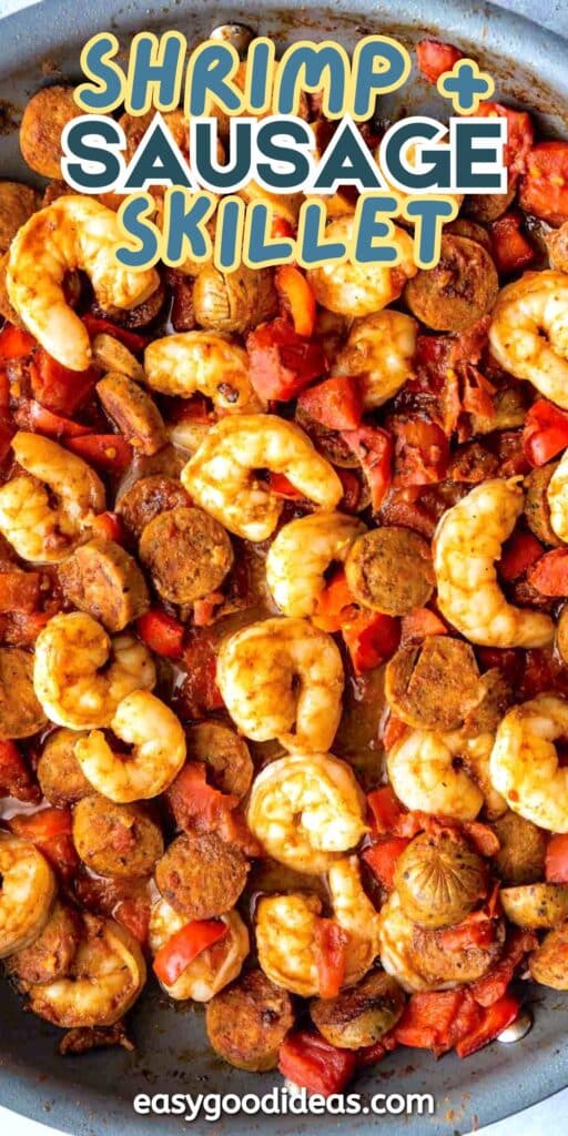 A close-up of a skillet filled with cooked shrimp, sliced sausage, red bell peppers, and seasonings. Text on the image reads Shrimp + Sausage Skillet and easygoodideas.com.