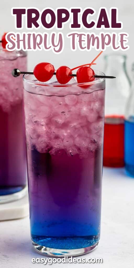 A tall glass of ice-filled, purple and blue layered drink is garnished with three maraschino cherries on a skewer. The text Tropical Shirly Temple appears at the top. Bottles with colorful liquids are blurred in the background.